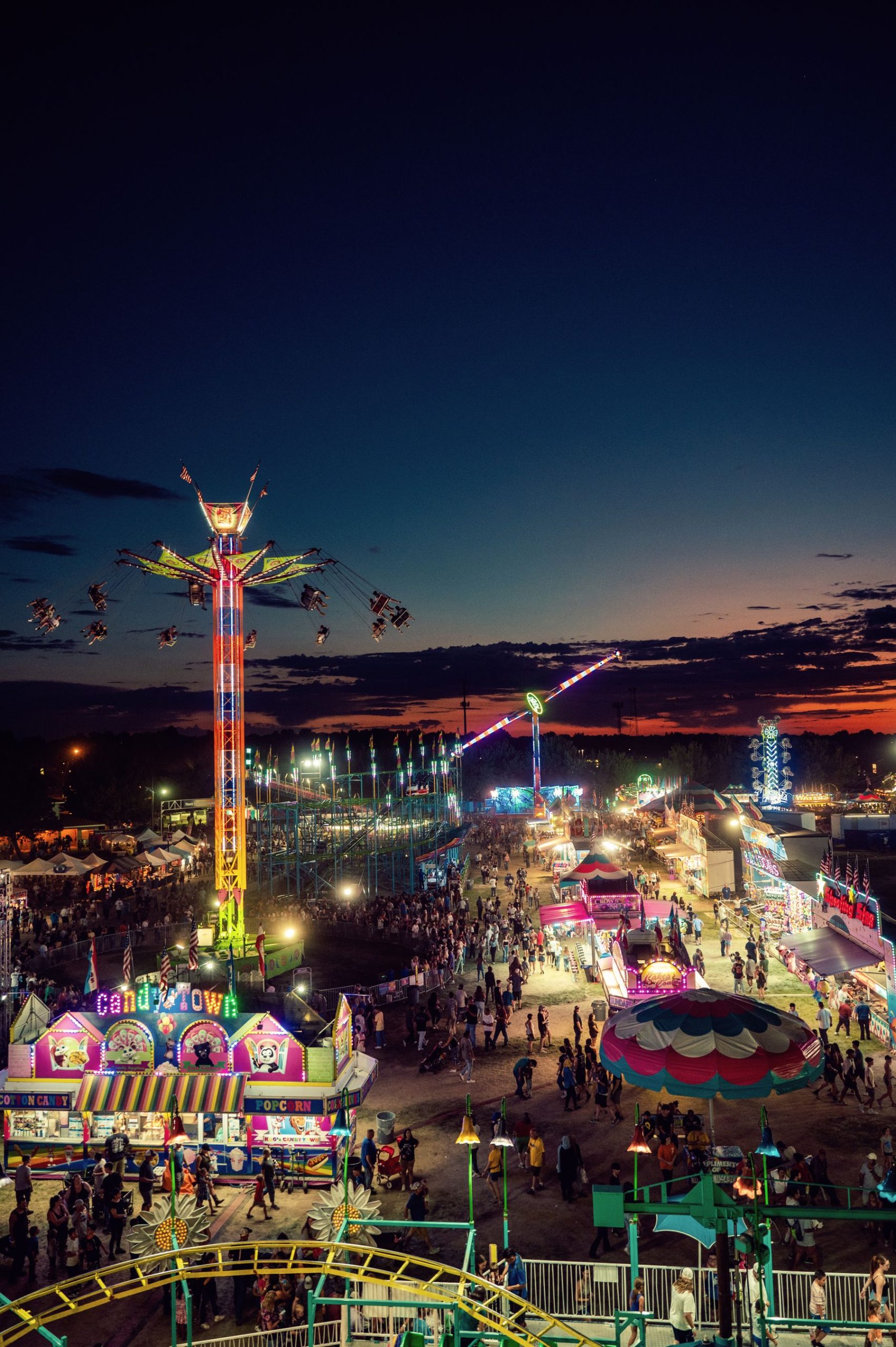 A busy fairground with rides glowing at dusk