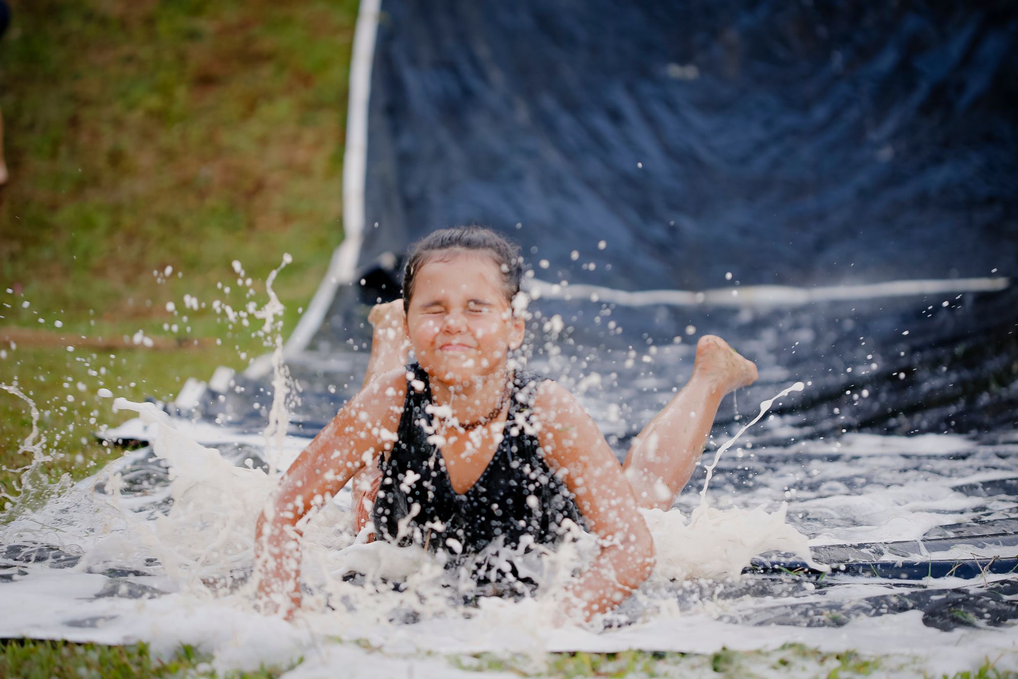 A laughing girl sliding through the water on a backyard slip-and-slide