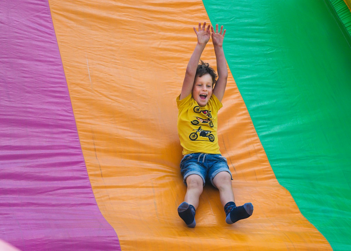 A boy cheering on his way down an orange inflatable slide