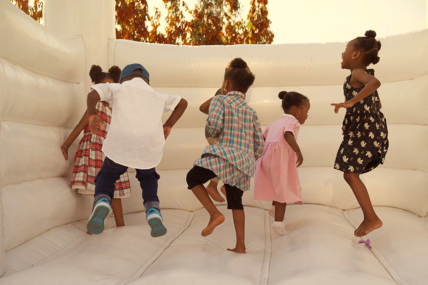 Kids jumping in a white bounce house under fall trees